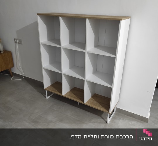 ארון מדפים לבן עם מדפי עץ, עומד על רצפה אפורה